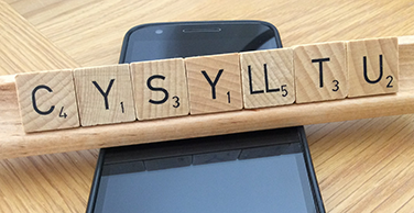 Mobile phone and the word 'cysylltu' (contact) on Scrabble tiles